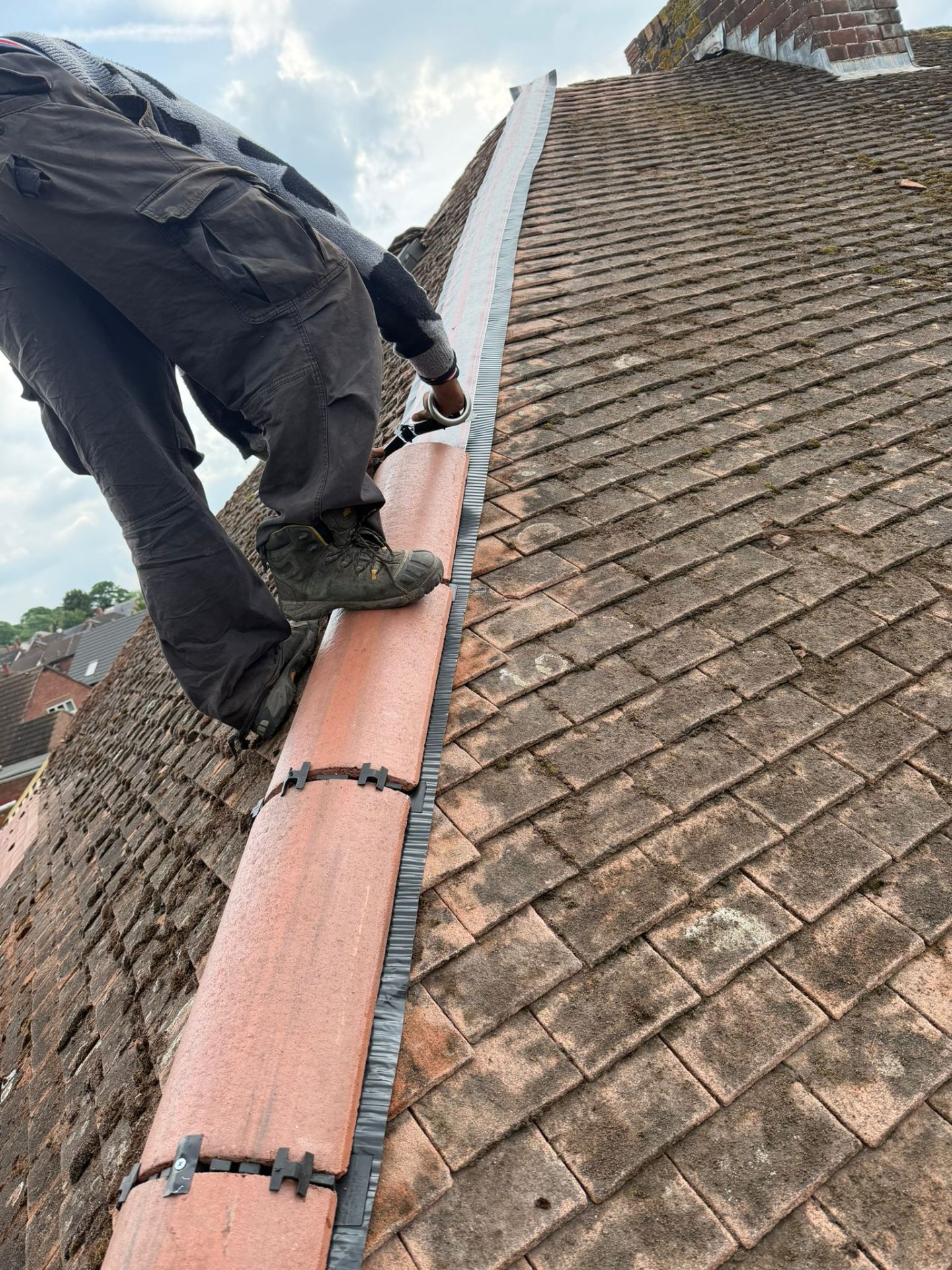Roofer re-bedding a clay ridge tile during a pitched roof repair in Worcestershire